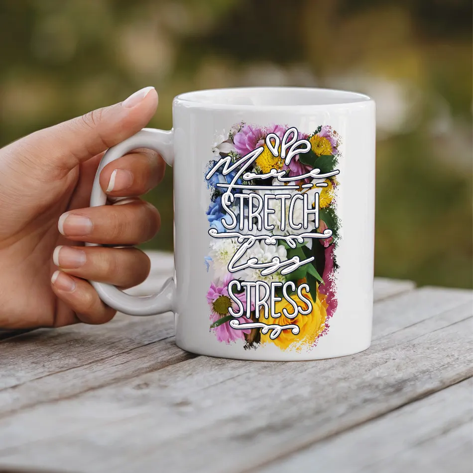White ceramic mug with a colorful floral design and bold white text that reads "More Stretch Less Stress".