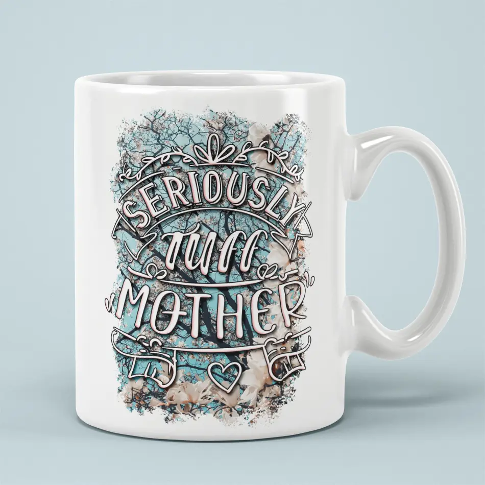 White ceramic mug with the text "SERIOUSLY TUFF MOTHER" in decorative font, set against a floral and tree branch background.
