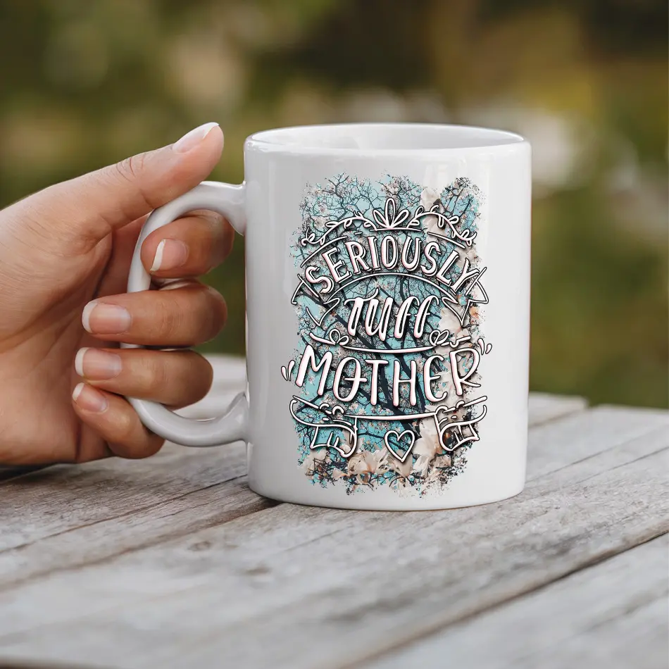 White ceramic mug with "SERIOUSLY TUFF MOTHER" text and a blue and brown abstract background.