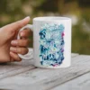 White ceramic mug with 'Strike A Pose' text over a floral background in shades of blue, teal, and pink.