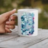 White ceramic mug with colorful floral design and text 'Sweating My Asana Off'.