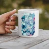 White ceramic mug with a floral design and text that reads 