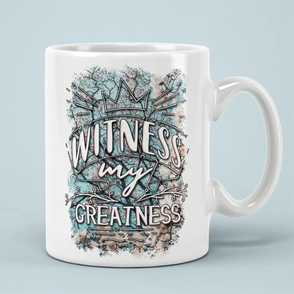 White ceramic mug with a crown and floral design, reads "Witness My Greatness".