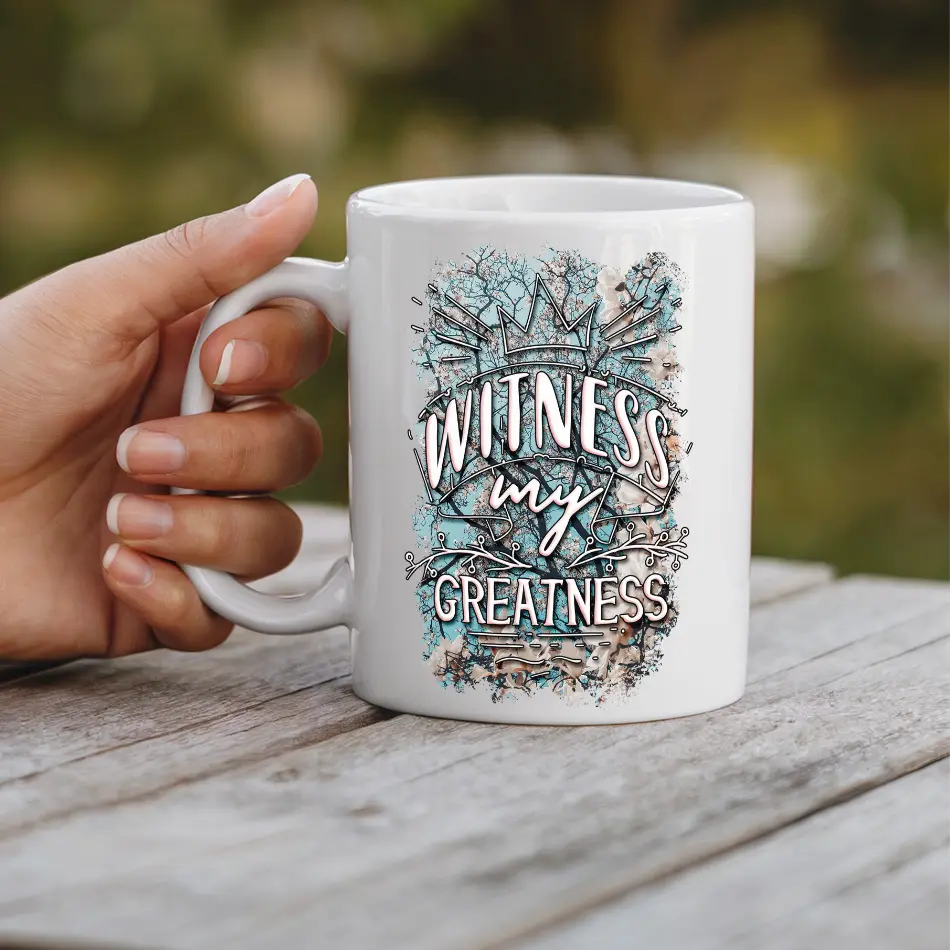 White ceramic mug with a crown design and text "WITNESS my GREATNESS" in a distressed, watercolor style.