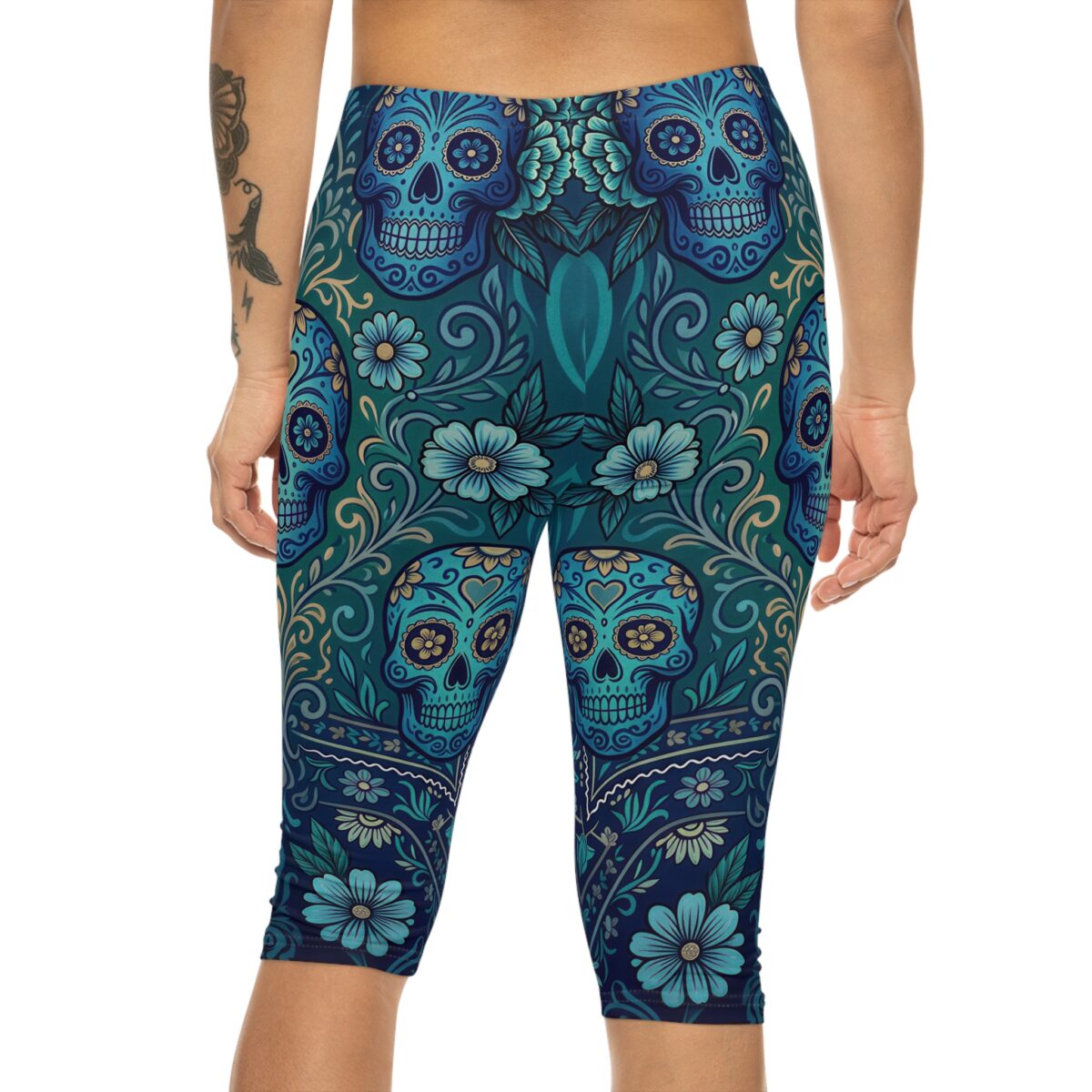 A person wears blue capri leggings featuring a pattern of sugar skulls and floral designs.