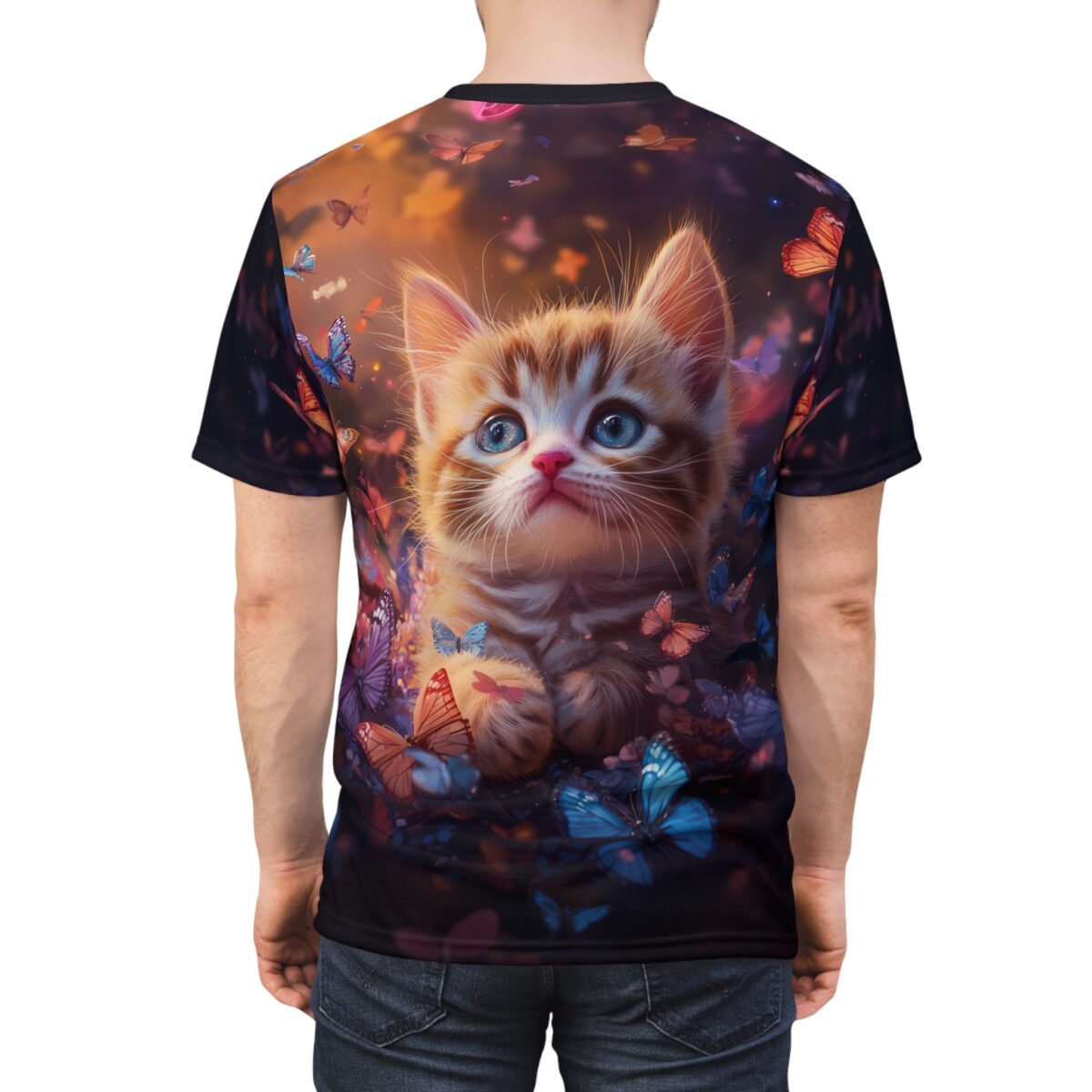 A graphic t-shirt features a close-up of a fluffy ginger kitten with striking blue eyes, nestled amongst colorful butterflies and dark foliage. The background is a warm blend of orange and purple hues.