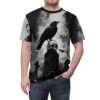 Black sublimation tee features a gothic scene with a raven perched on a skull atop a tombstone, with bats and crosses in the background.