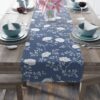 Blue table runner featuring a repeating white floral and branch pattern. Perfect for elegant dining and home decor.