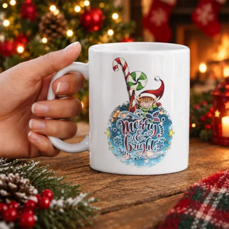 White ceramic coffee mug decorated with a whimsical Christmas elf, candy cane, and Merry & Bright typography graphic.