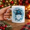 White ceramic coffee mug featuring a blue patterned winter gnome and snowflakes with holiday text design.