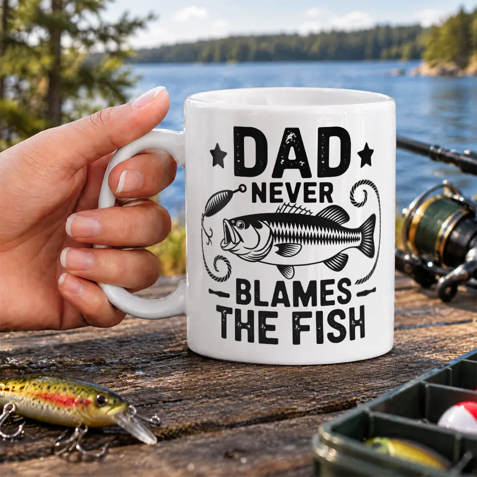 White ceramic mug featuring bold black lettering reading Dad Never Blames The Fish with a detailed bass graphic.