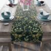 Dark green table runner featuring a repeating holly leaf and berry pattern with gold accents, perfect for holiday decor.