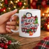 Festive Merry Christmas ceramic mug featuring a smiling snowman, red buffalo plaid background, green trees, and golden bell graphic.