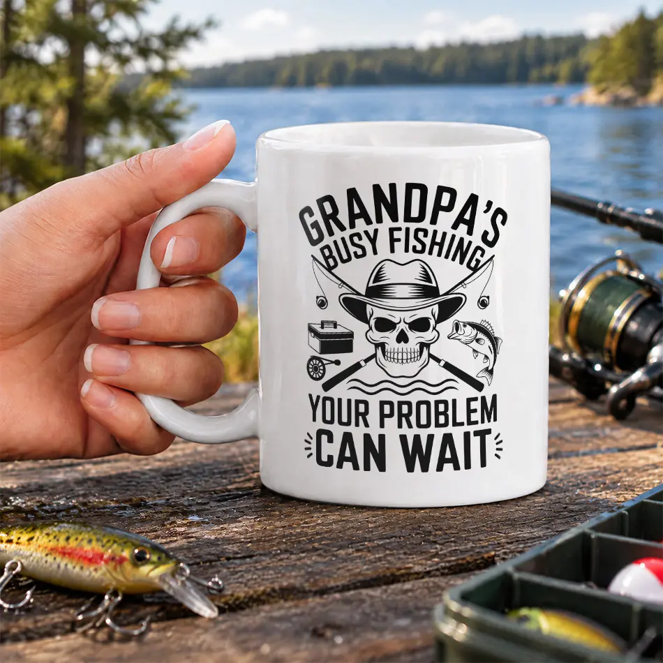 White ceramic fishing mug printed with a hat-wearing skull, fishing rods, bass, and funny grandpa text.