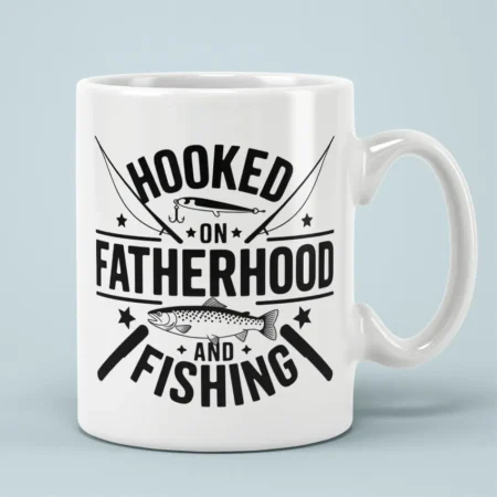 White ceramic coffee mug printed with black text reading Hooked on Fatherhood and Fishing alongside fish graphics.