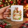 White ceramic mug displaying a Christmas elf holding a gift with Merry and Bright golden script lettering.