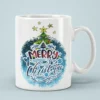White ceramic coffee mug featuring Merry Christmas lettering with a decorated Christmas tree and blue splatter background.