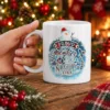 White ceramic coffee mug featuring a snowman graphic with Proud Member Of The Naughty List festive typography.